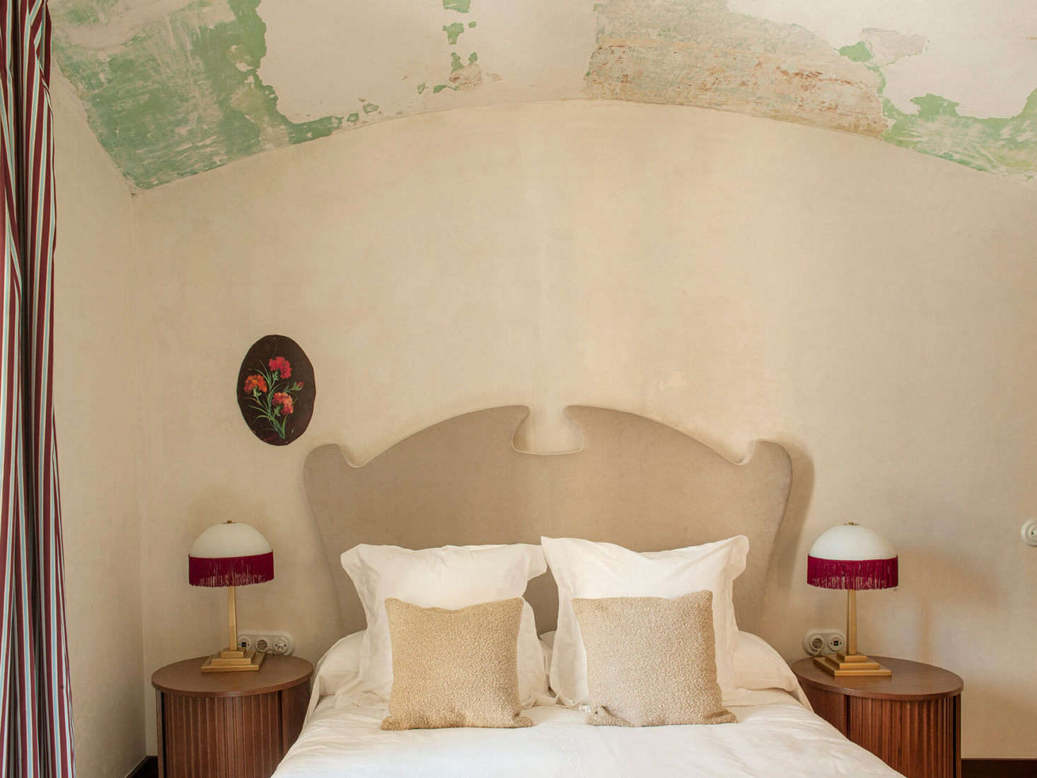 Under an atmospheric raw ceiling, a fanciful headboard flanked by fringed lamps.
