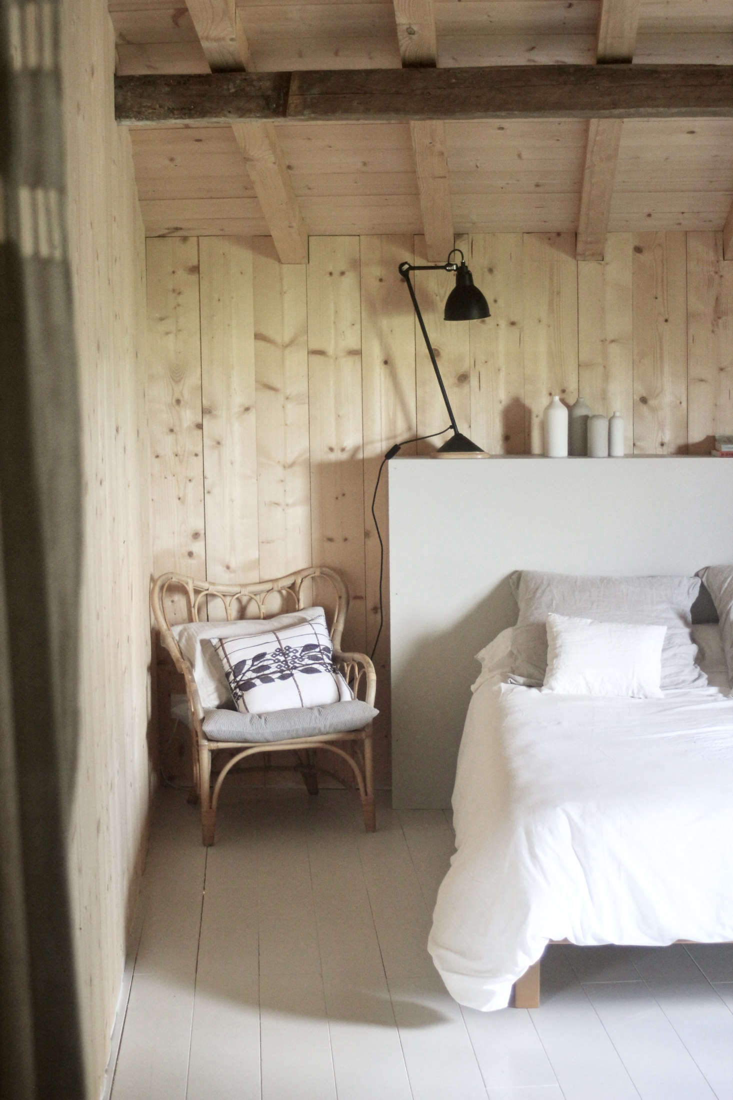 The bedrooms are paneled in pine boards salvaged from the roof and have wooded floors painted, like the homemade headboard, are in Farrow & Ball