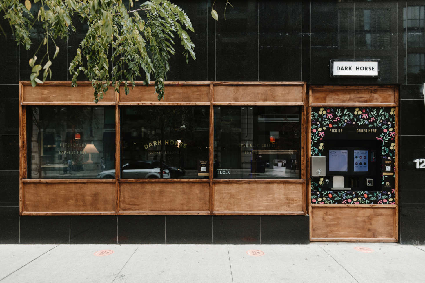 The facade features an outdoor ordering station; passersby can peer through the window at the stage-set-like coffee shop interior.