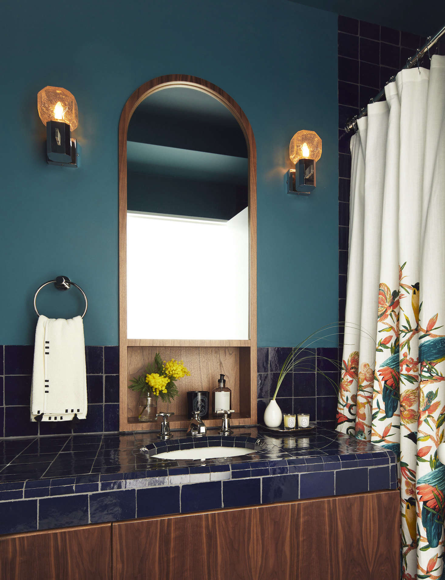 In the guest bath, the walnut millwork and mirror were custom-designed by Frederick Tang Architecture. The zelig tiles are from Mosaic House; the German theater wall lights are by Cosack from data-src=