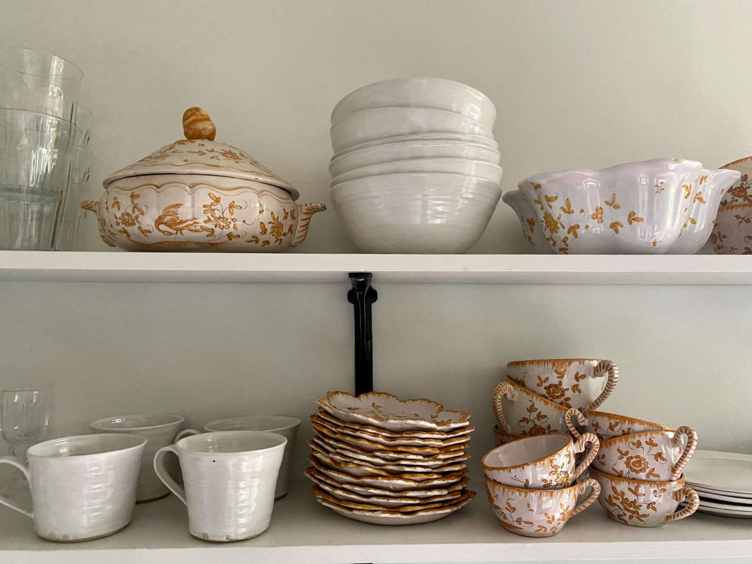 Her collection of gold and pink Moustiers faience earthenware, found at an auction, sit on open shelves.