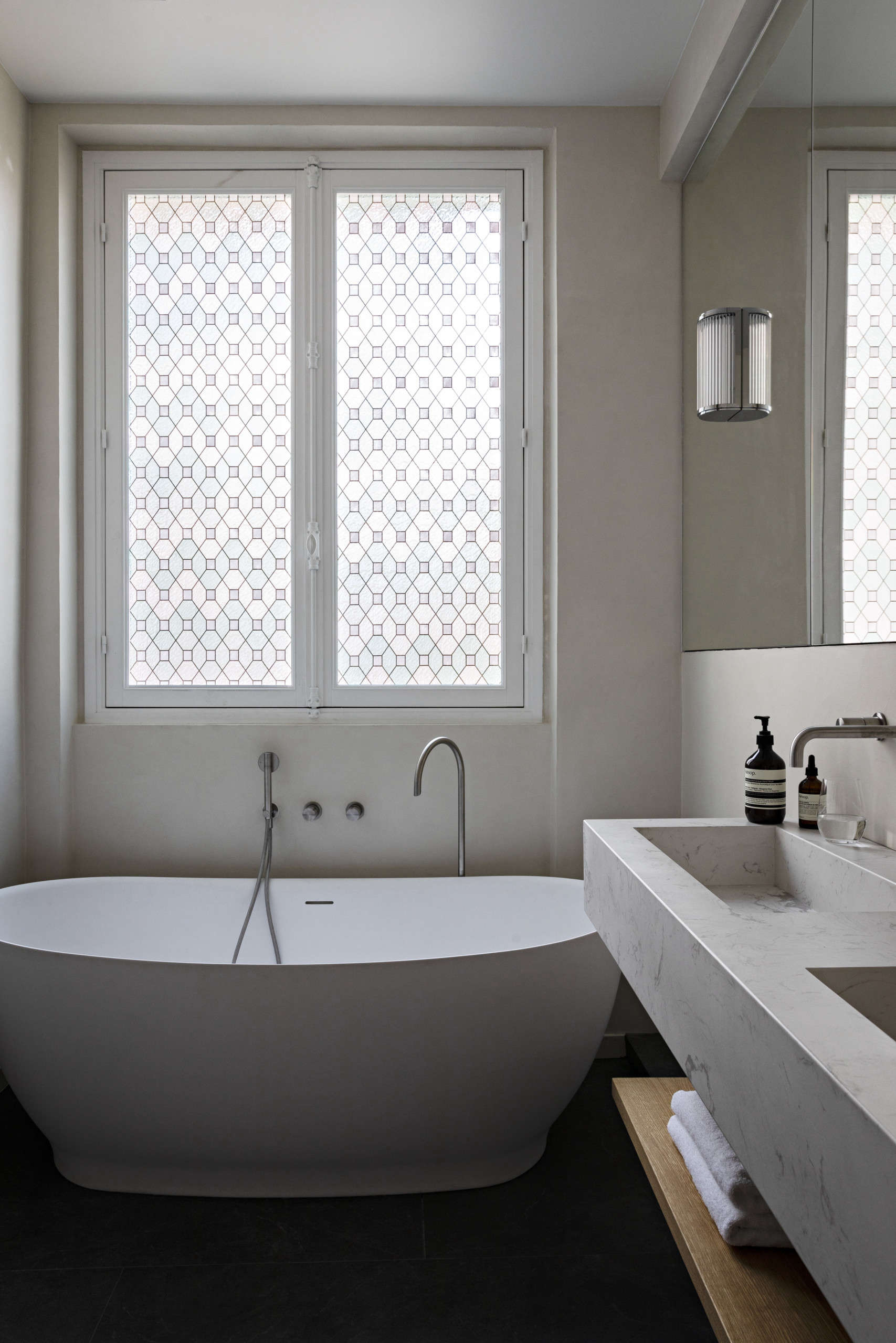 The multiple shades of white in the bathroom make the space feel like a serene oasis. The wall light on the mirror is the Versailles 0 LED from Astro and the faucet is from Neve Rubinetterie.