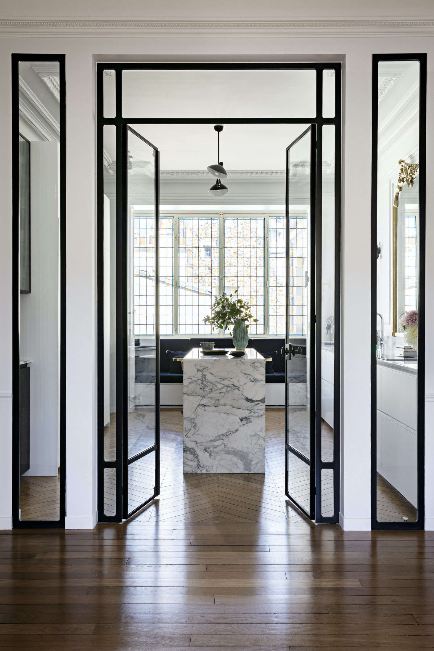 Revolving around a center island, the kitchen incorporates walnut, marble, and metal into the design. Tall glass doors open up to the space.