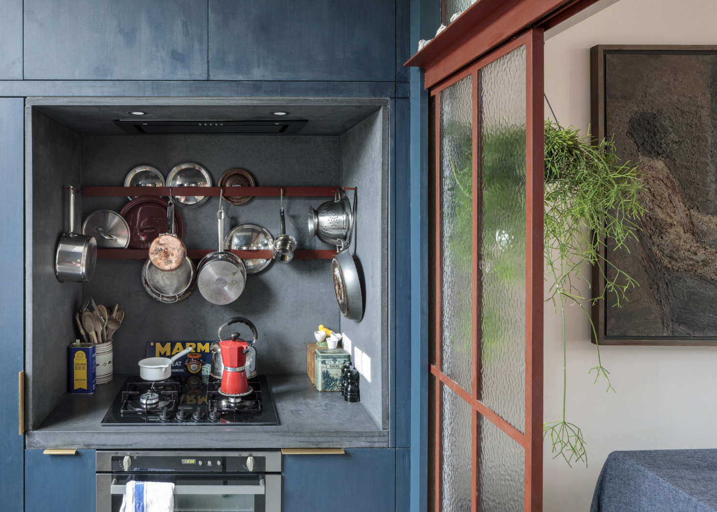 The compact cooking niche has a concrete surround made by Kast. The custom cabinets are blue-stained spruce: 