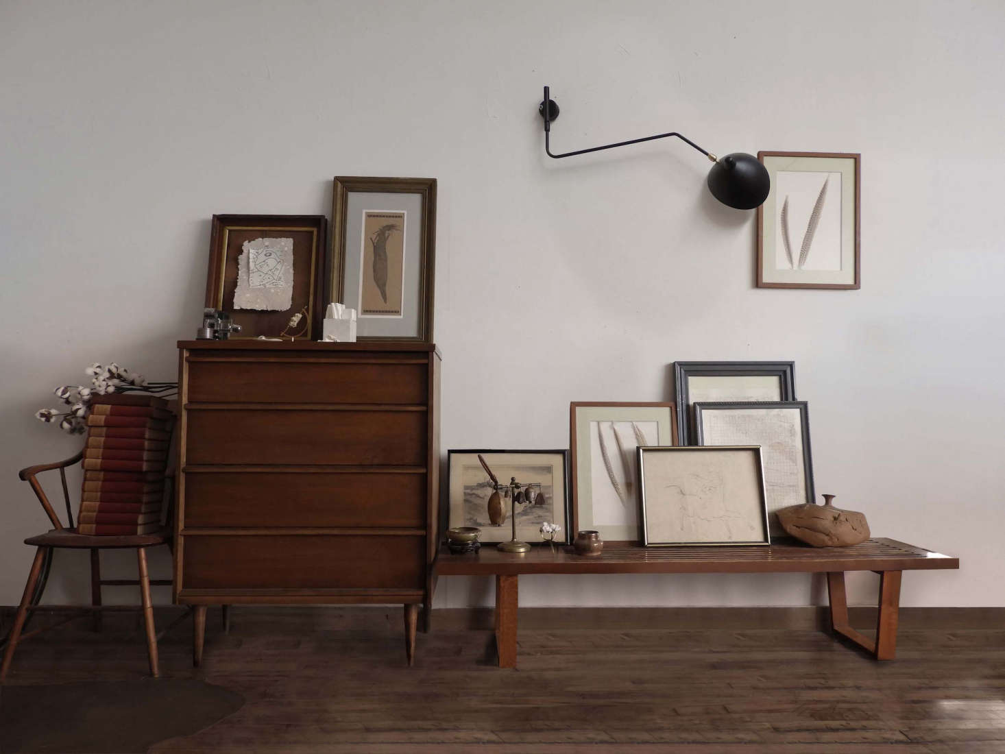 A vintage Serge Mouille light hangs above a collection of framed artwork, casually propped against the wall on a Nelson-style bench. The dresser is a hand-me-down from Jeff