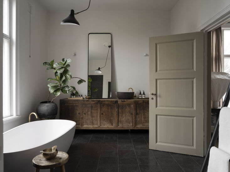 a bathroom outfitted with black tile, a freestanding tub, antique console, fidd 28