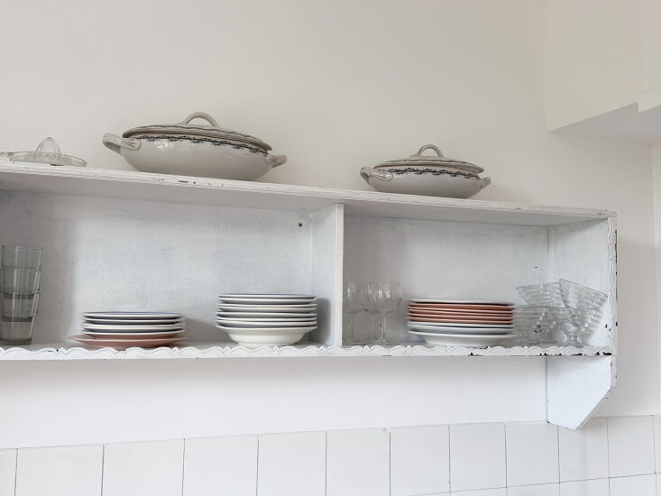 a painted wooden shelf displays vintage glassware, plates, and serving pieces†25